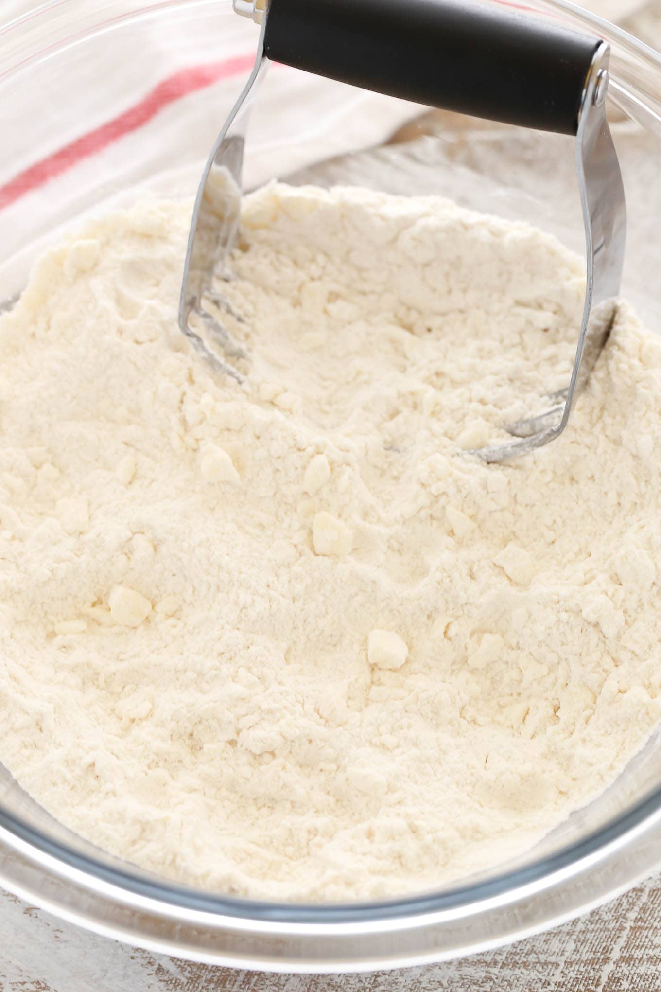 A pastry cutter in a glass mixing bowl of flour and butter. 