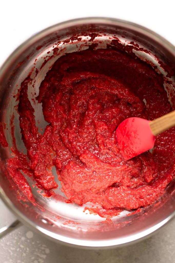 An overhead view of reduced strawberry puree in a saucepan. A rubber spatula rests in the pan. 