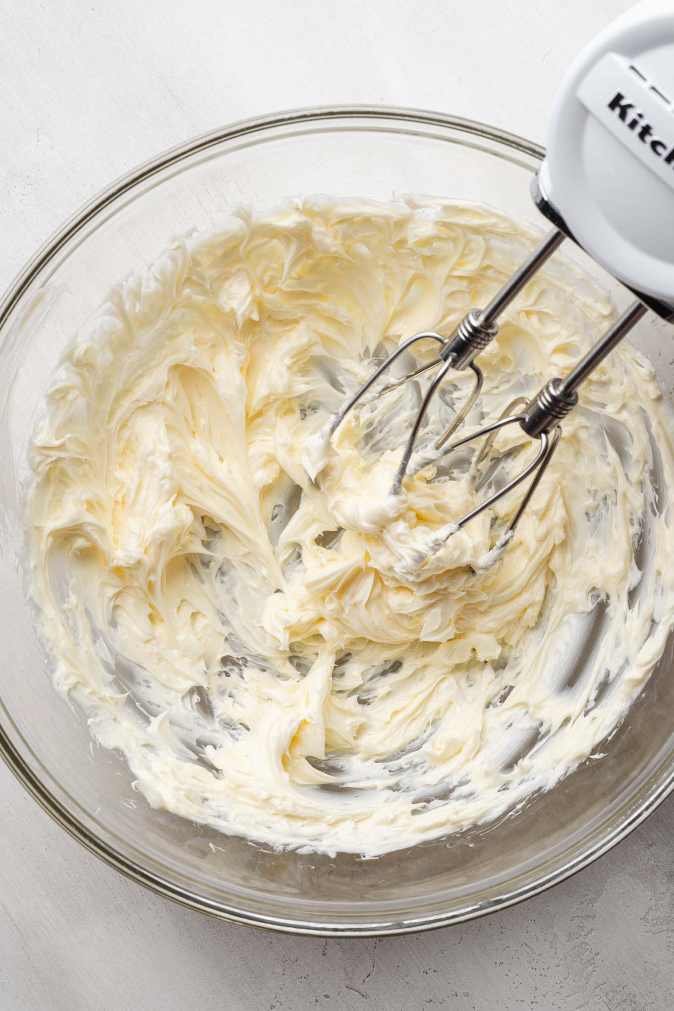 An overhead view of creamed butter in a glass mixing bowl with a hand mixer.