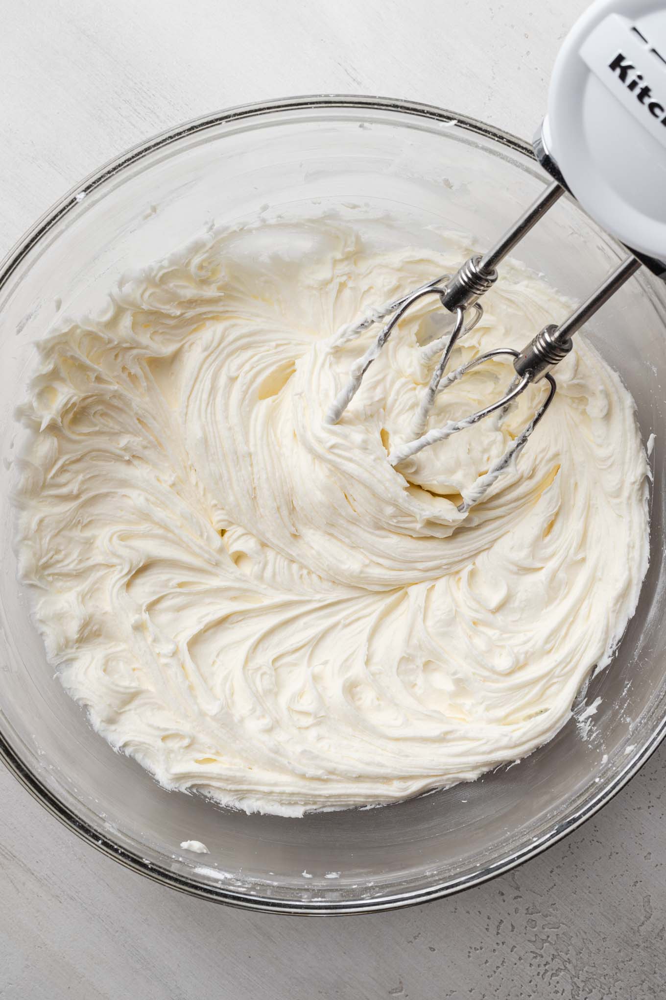 An overhead view of creamed butter and sugar in a glass mixing bowl with a hand mixer.