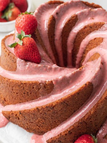 A strawberry pound cake topped with strawberry icing. A few strawberries rest on top of the cake.