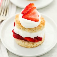 Strawberry shortcake topped with extra whipped cream and strawberries on a white plate.