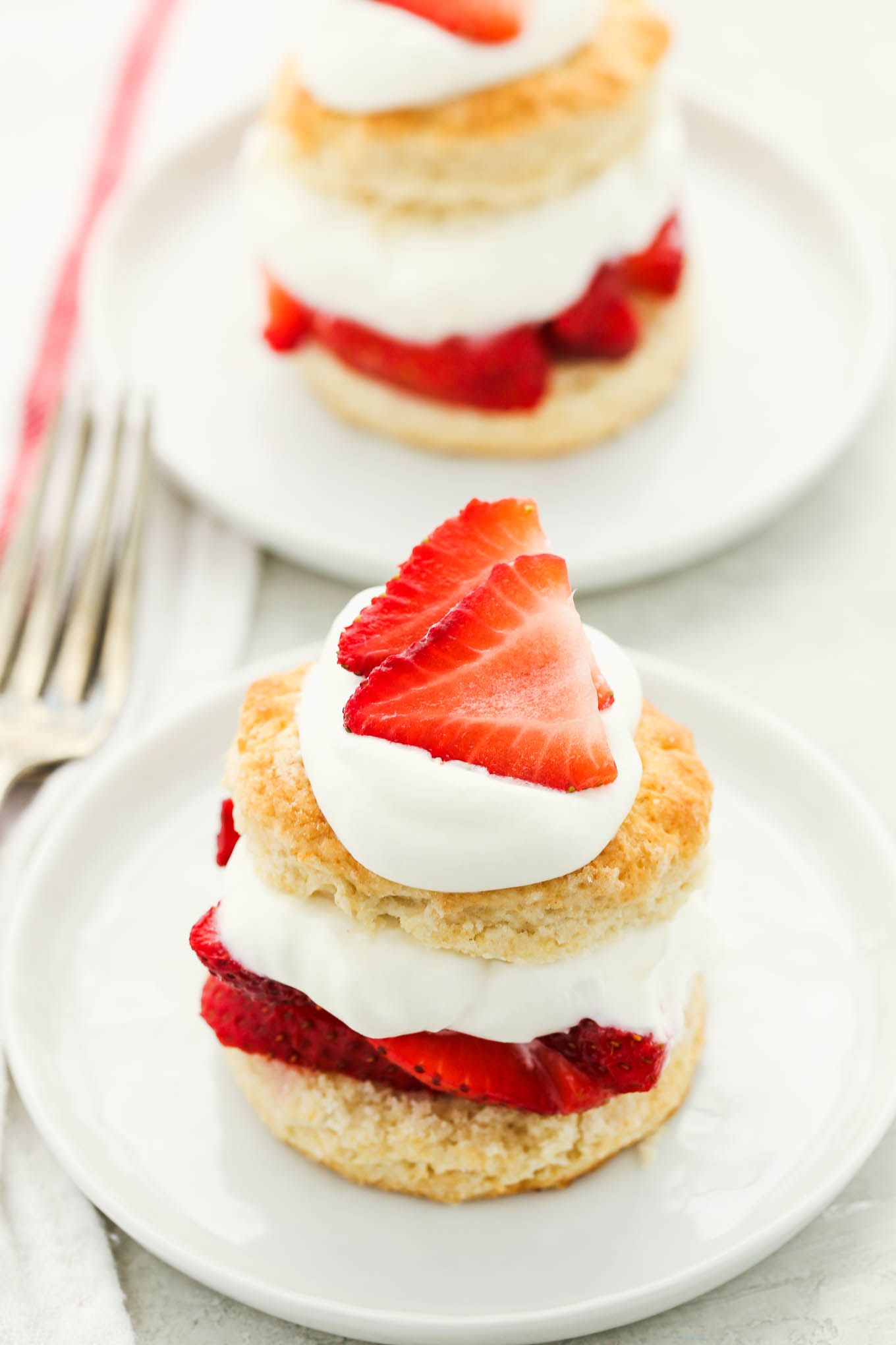 Two prepared strawberry shortcakes topped with extra whipped cream and sliced strawberries on white plates.