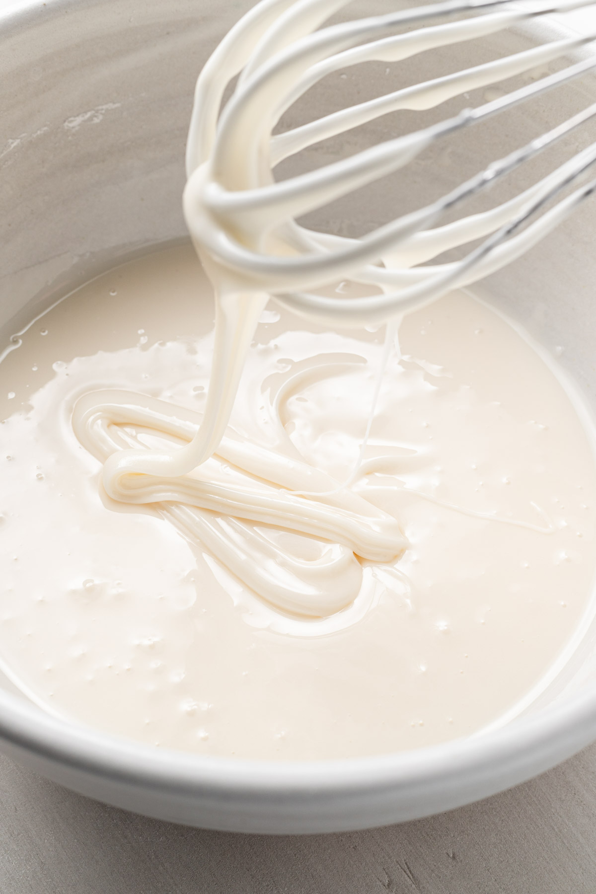 A bowl of sugar cookie icing with a whisk held over it to show the outline consistency.