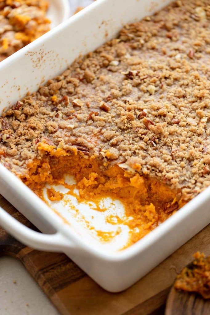 A sweet potato casserole in a baking dish with one corner scooped out to show the sweet potato base.