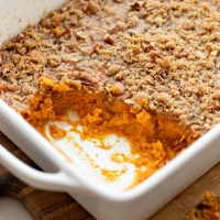 A sweet potato casserole in a baking dish with one corner scooped out to show the sweet potato base.