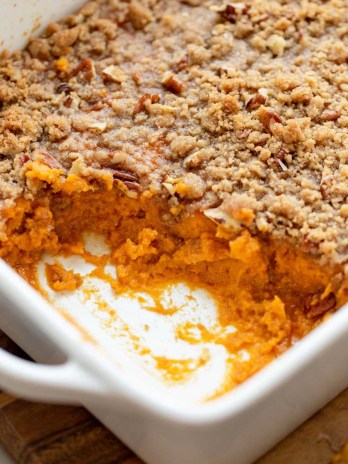 A sweet potato casserole in a baking dish with one corner scooped out to show the sweet potato base.