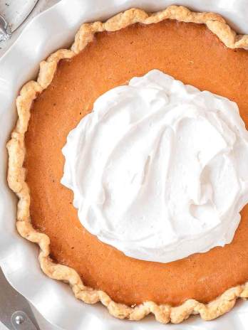 An overhead view of a sweet potato pie topped with homemade whipped cream in a white pie dish.