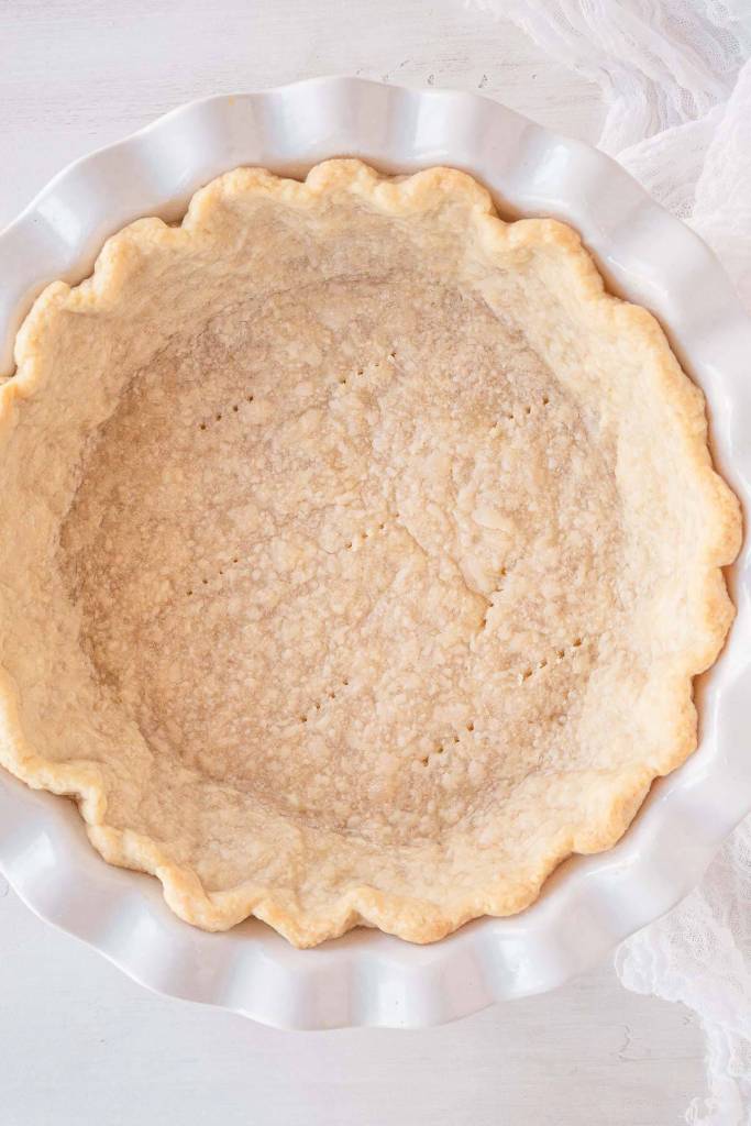 An overhead view of a partially baked pie shell in a pie plate. 