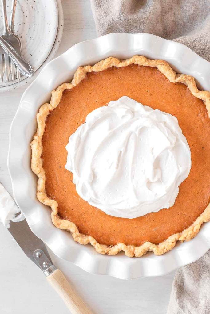 An overhead view of a baked sweet potato pie garnished with whipped cream in a white plate plate. 