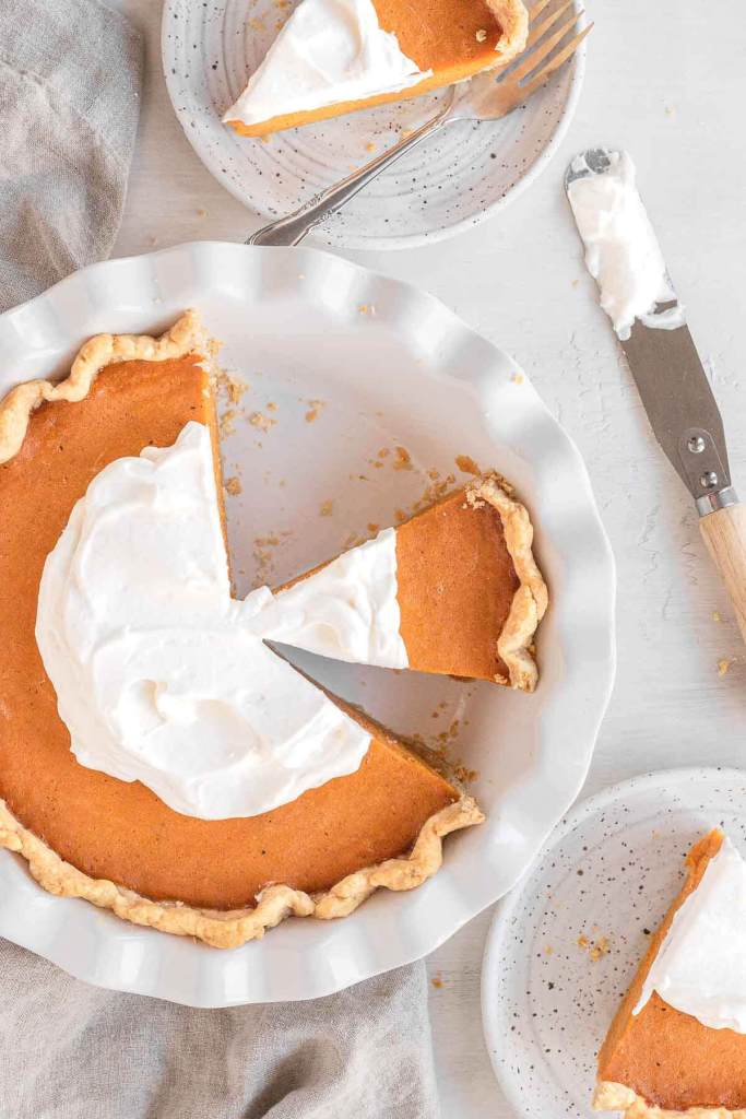 An overhead view of a homemade sweet potato pie garnished with whipped cream. Two slices have been remove and another rests in the pie plate. 