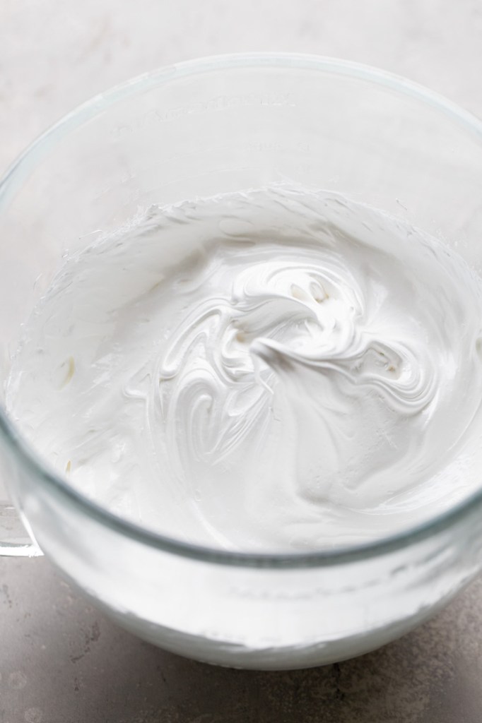 An overhead view of egg whites that have been whipped to stiff peaks in a glass mixing bowl. 