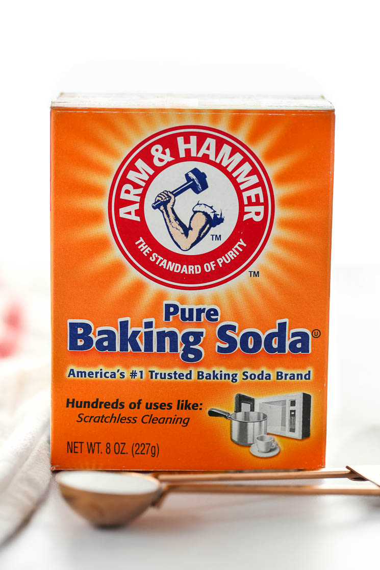 A box of baking soda behind a measuring spoon on top of a marble surface. 