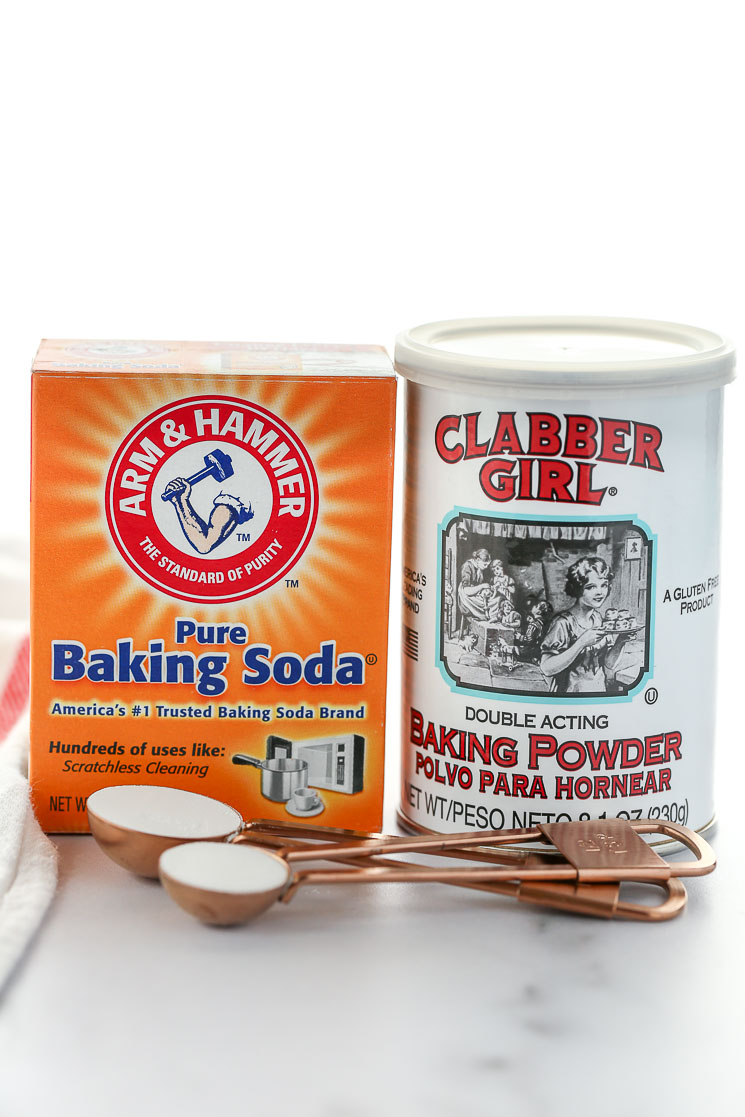 A box of baking soda and can of baking powder on top of a marble surface.