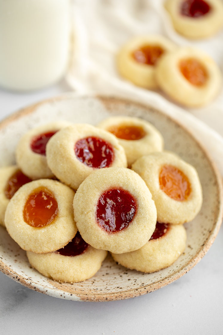Thumbprint cookies sitting on top of a speckled place with more cookies behind it.