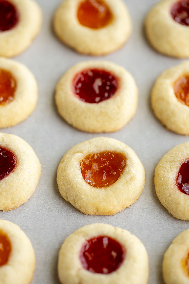 Baked thumbprint cookies lined up on a piece of parchment paper.
