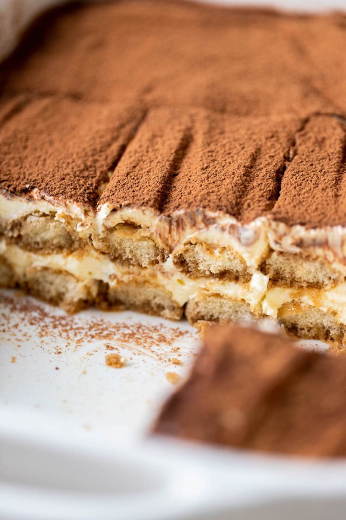 A baking dish of classic tiramisu. A few slices are missing from the front.