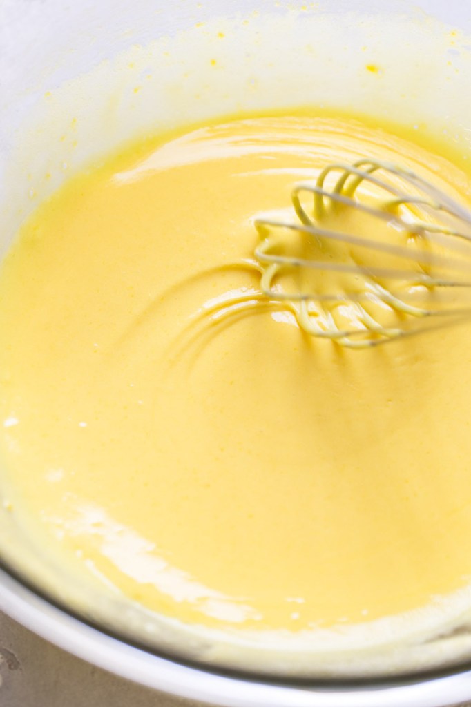 Egg yolk mixture being whisked in a glass bowl.