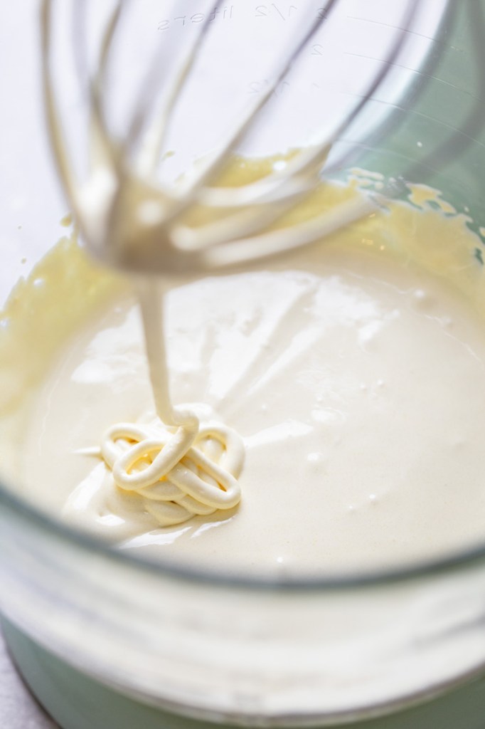 Tres leches cake batter in a glass mixing bowl. A whisk hangs over the bowl. 