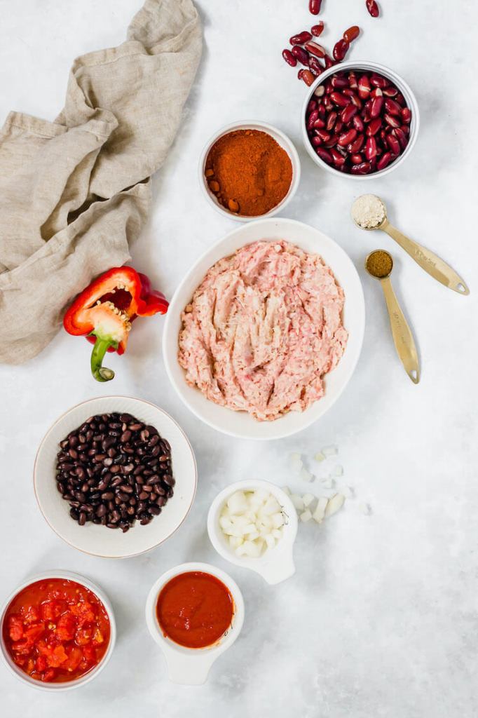 The ingredients needed to make turkey chili in different bowls on a gray surface.