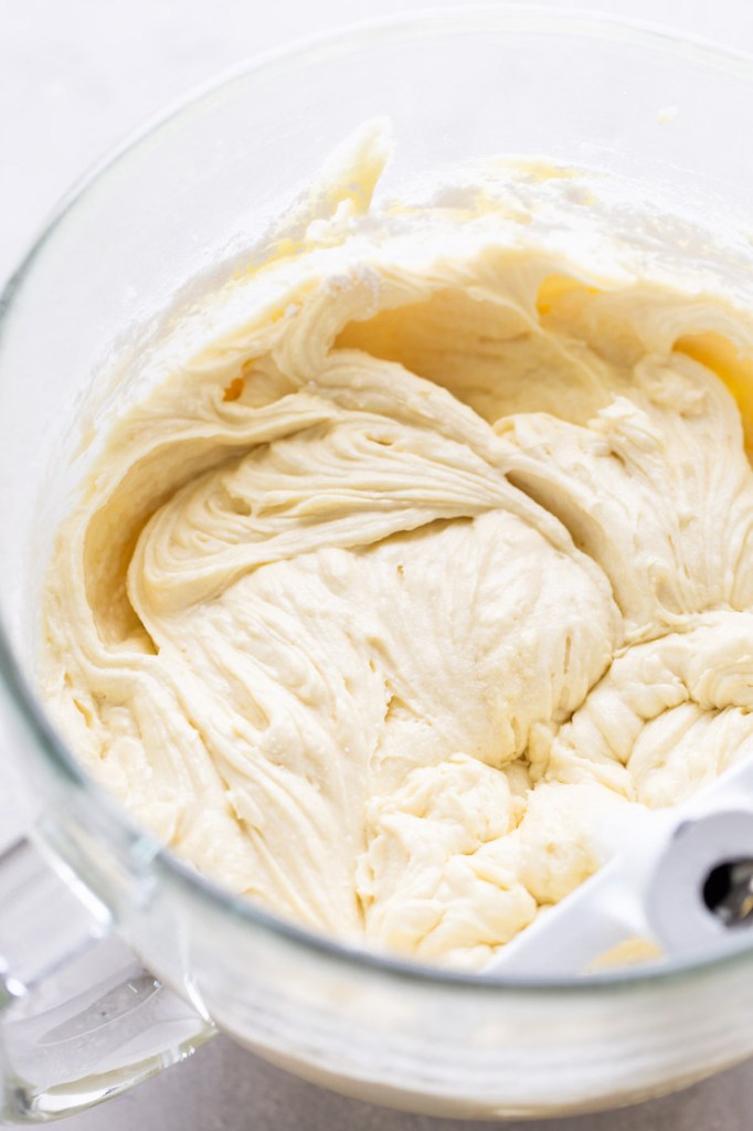 Vanilla cake batter in a glass mixing bowl. The paddle attachment of a stand mixer rests in the bowl. 