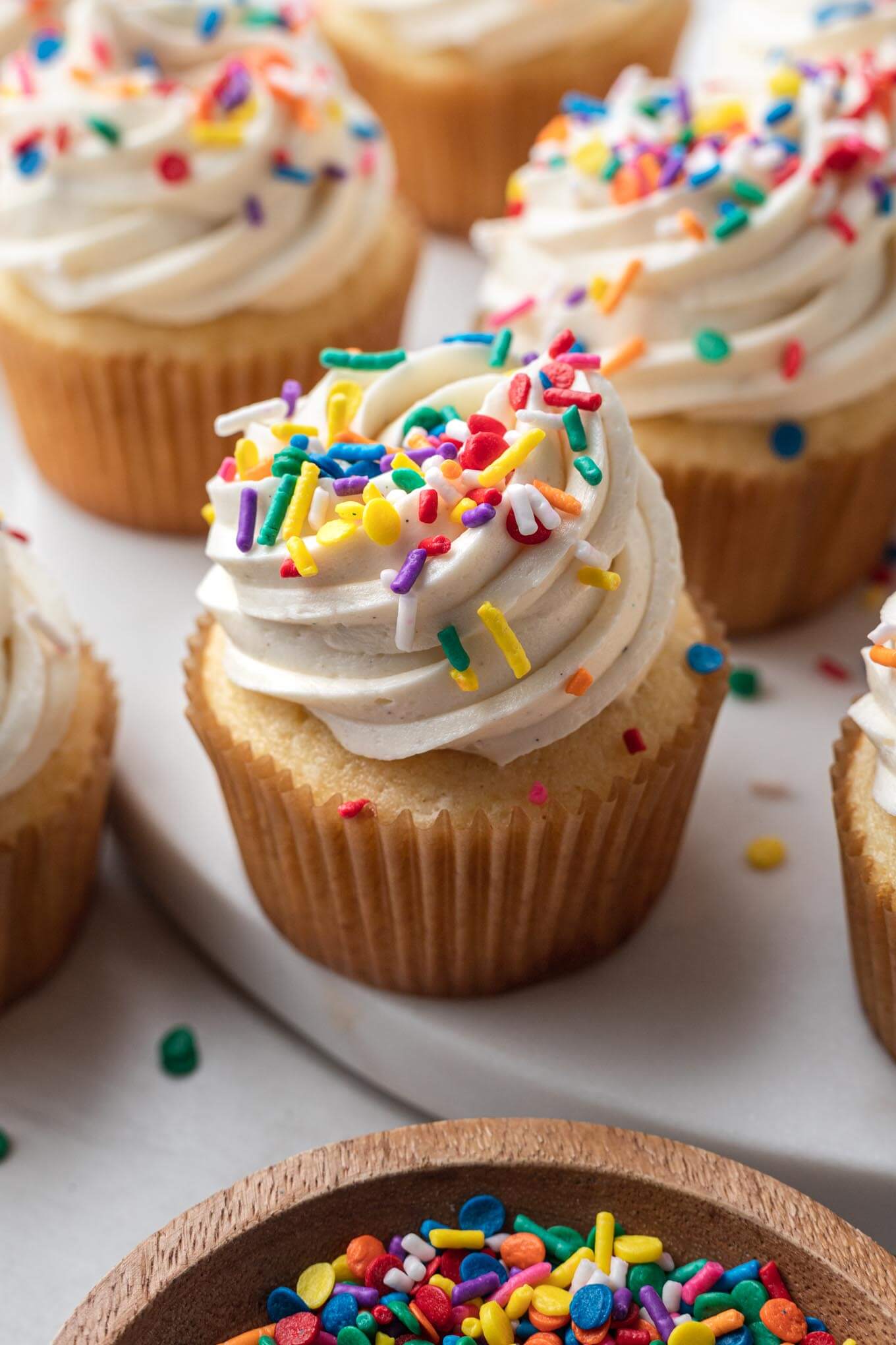 Homemade vanilla cupcakes topped with frosting and sprinkles. 