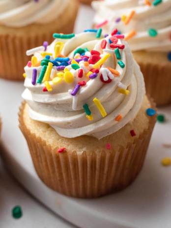 Vanilla cupcakes topped with sprinkles on a around marble serving platter.