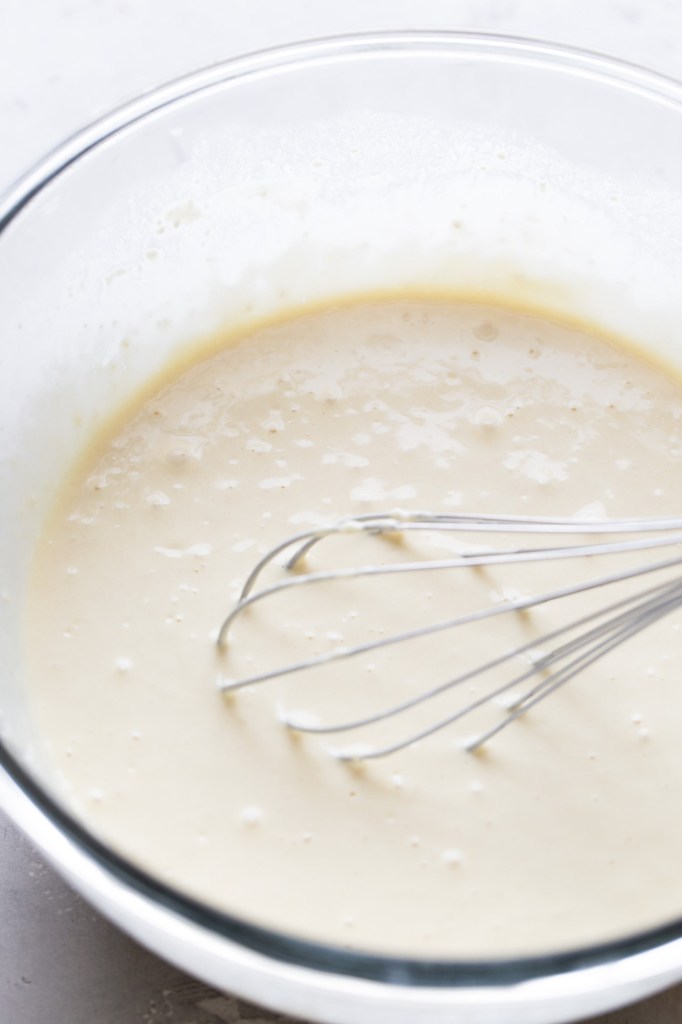 Waffle batter in a glass mixing bowl. A whisk rests in the mixing bowl. 