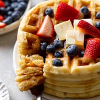 A tall stack of waffles topped with berries, butter, and syrup.