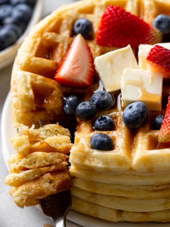 A tall stack of waffles topped with berries, butter, and syrup.