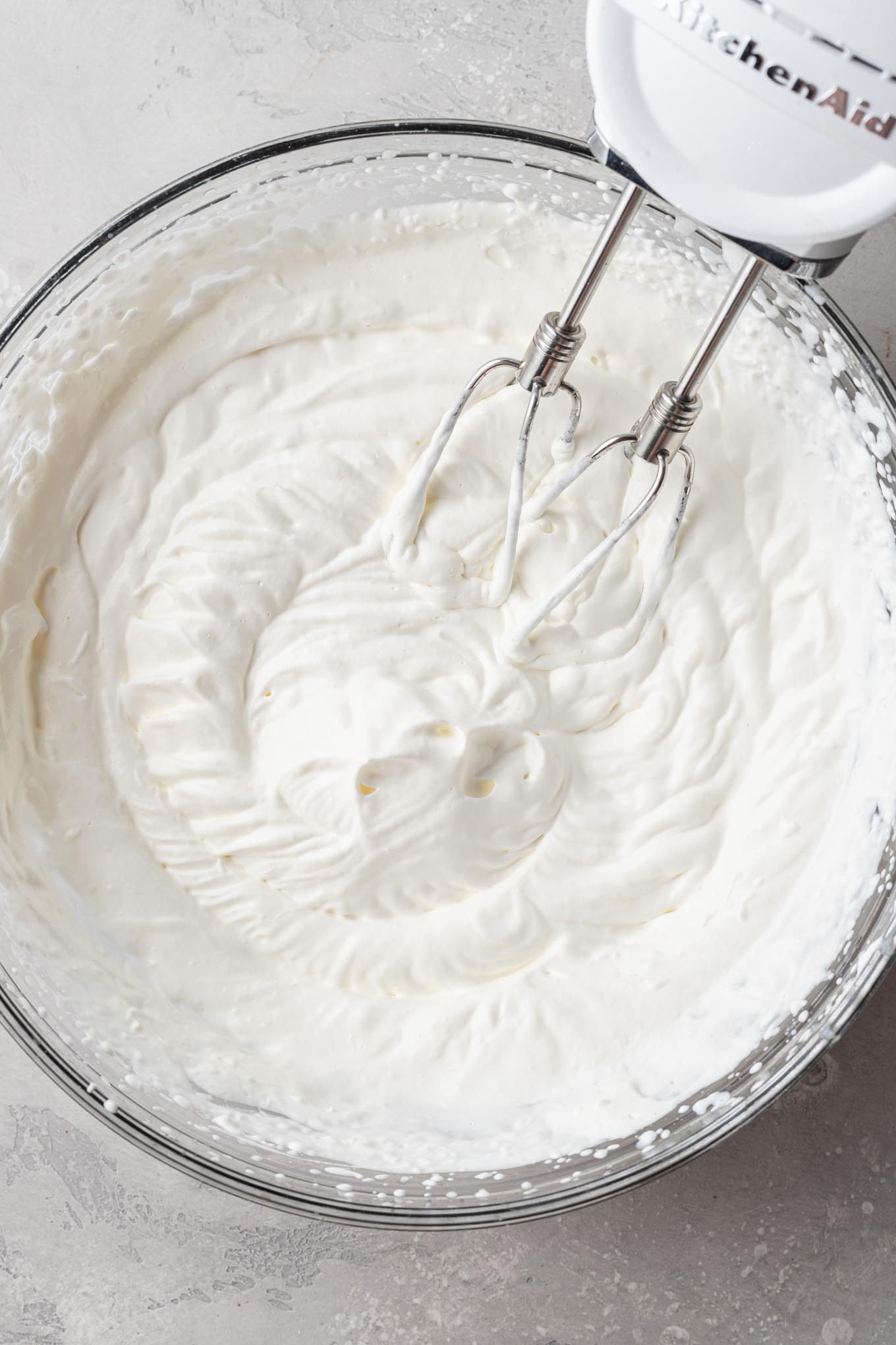 An overhead view of whipped cream beat to stiff peaks in a glass mixing bowl.