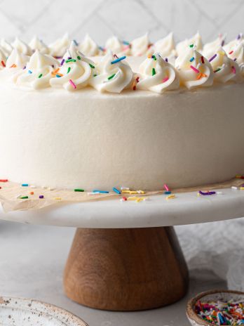 A white cake topped with sprinkles on a marble cake stand.
