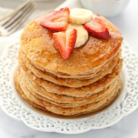 A stack of whole wheat pancakes topped with strawberry, banana slices, and maple syrup.