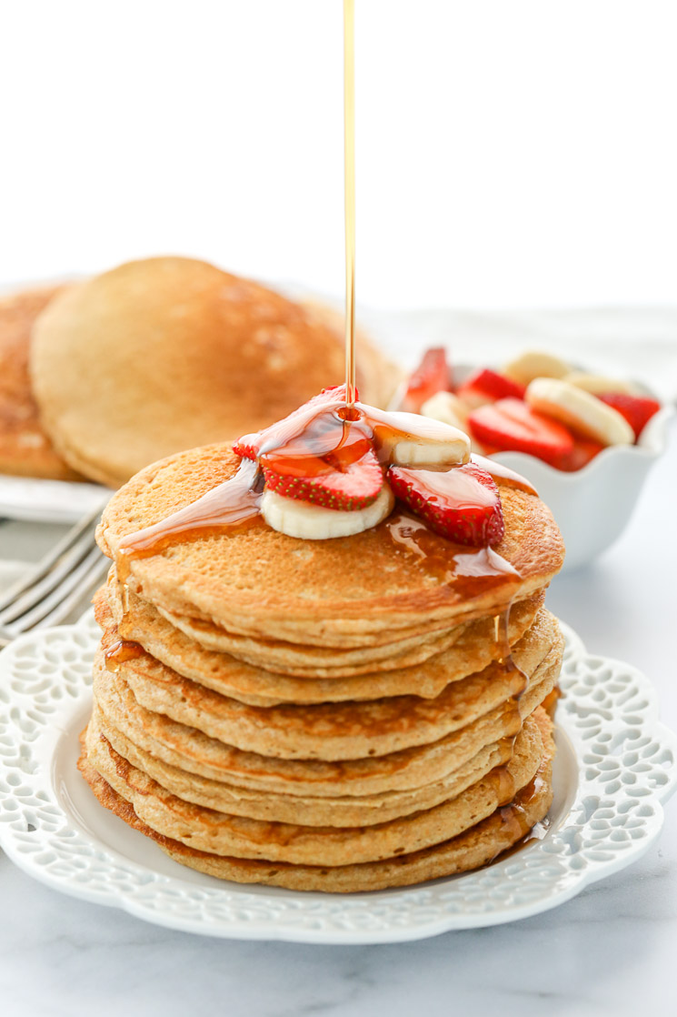 A stack of whole wheat pancakes topped with sliced strawberries and bananas drizzled with pure maple syrup.