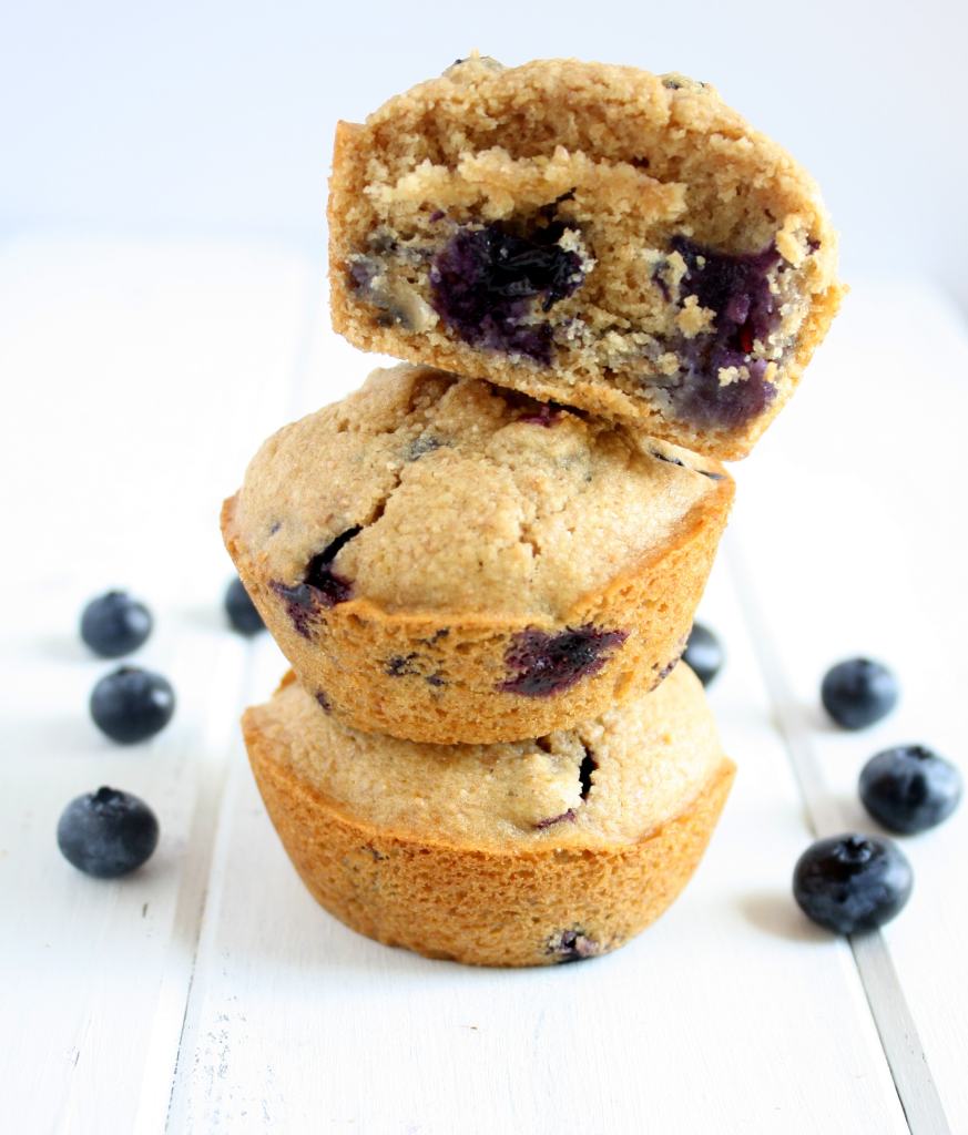 A stack of three whole wheat blueberry muffins. The top muffin has a bite missing.