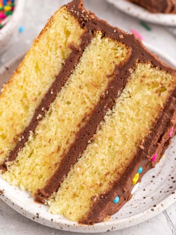 A slice of yellow cake on a white speckled plate.