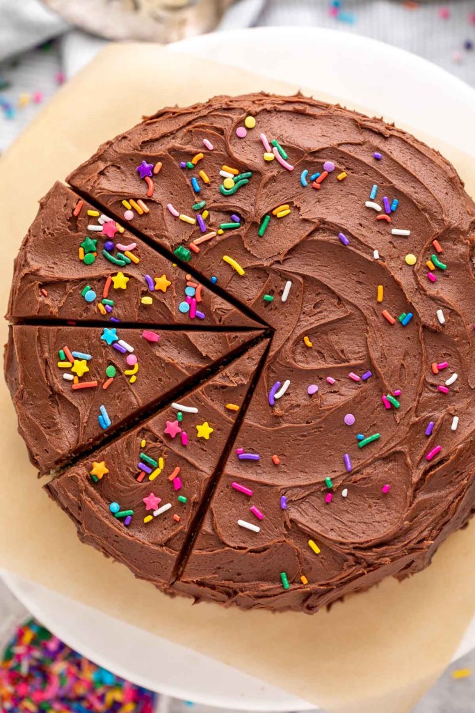 An overhead view of a yellow cake coated in chocolate buttercream frosting and topped with sprinkles.