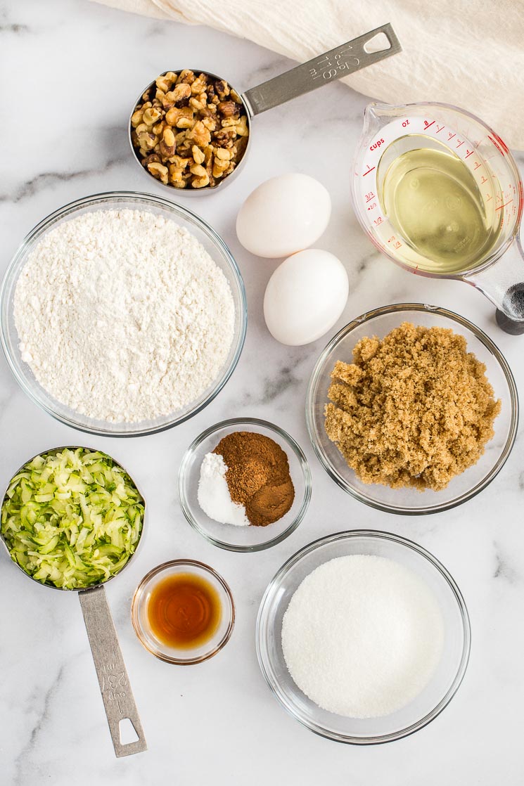 The ingredients needed for zucchini bread sitting on top of a marble surface. 