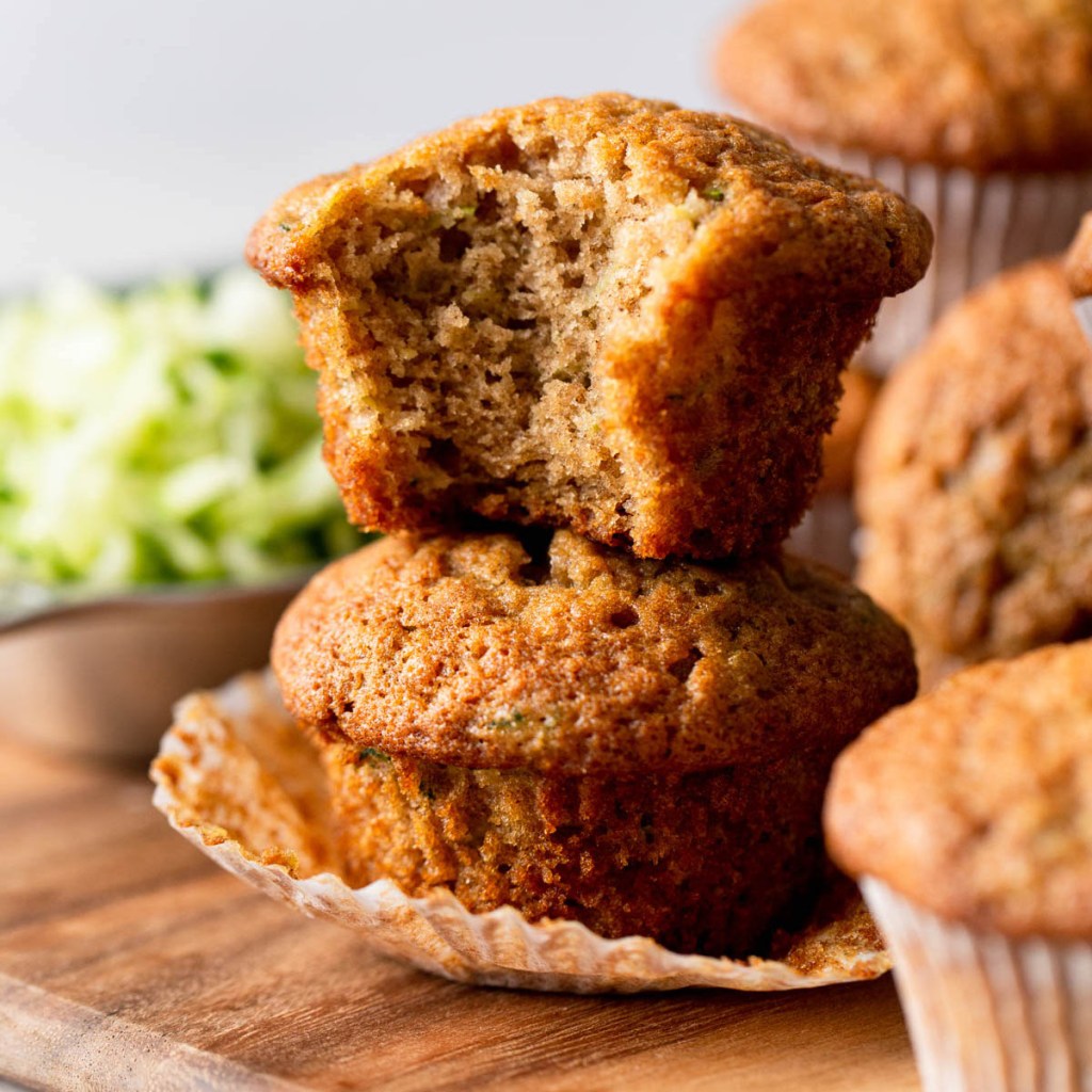 Two zucchini bread muffins stacked on top of each other. The top muffin has a bite missing. 