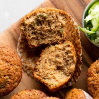 An overhead view of zucchini muffins on a wood cutting board. One muffin has been cut in half and others are lying on their sides.